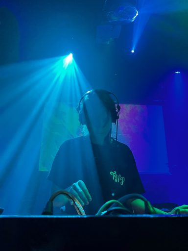 DJ achter een mengpaneel met gekleurd licht en stralen die de ruimte verlichten.